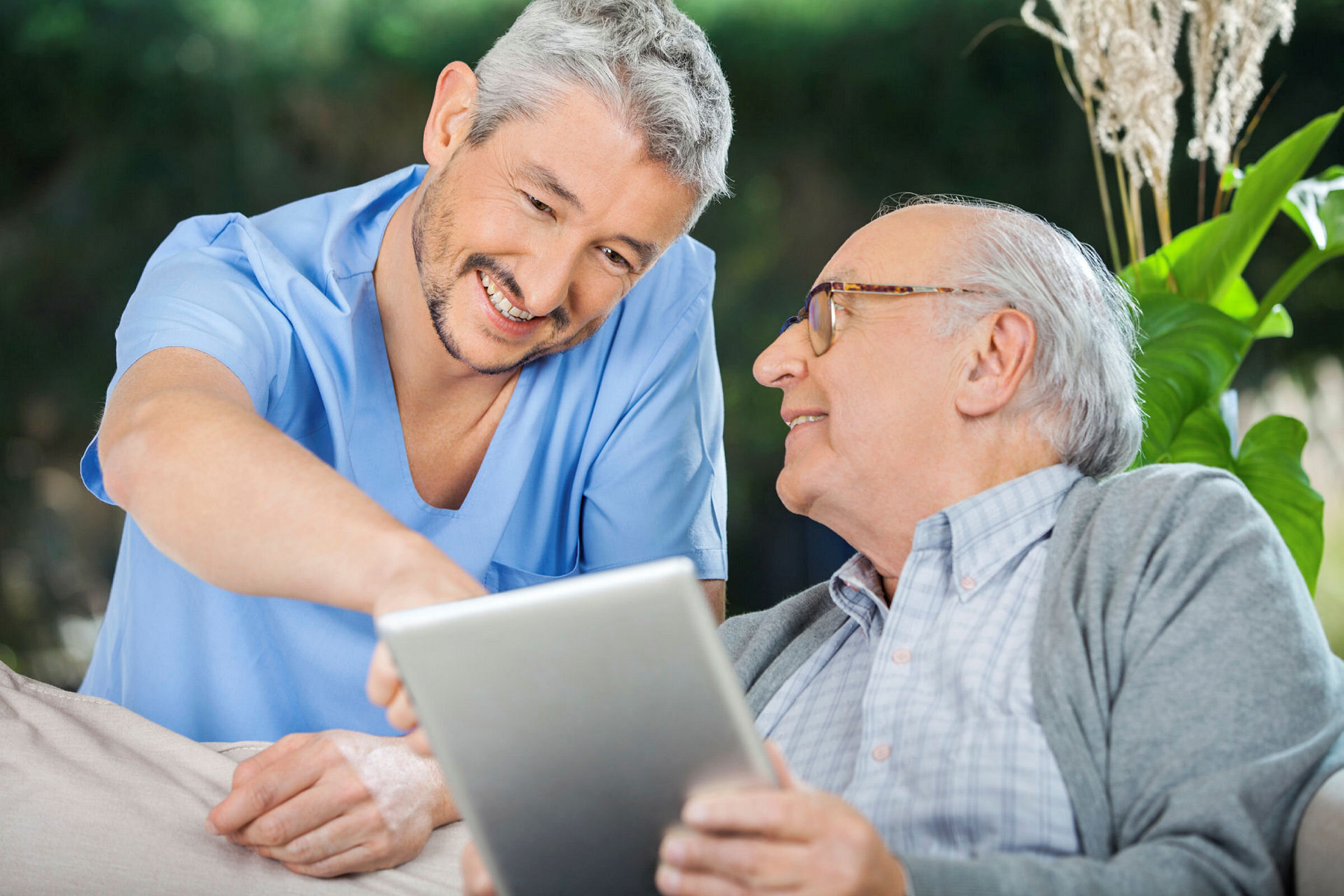 Sykepleier og eldre mann smiler og ser på ipad.