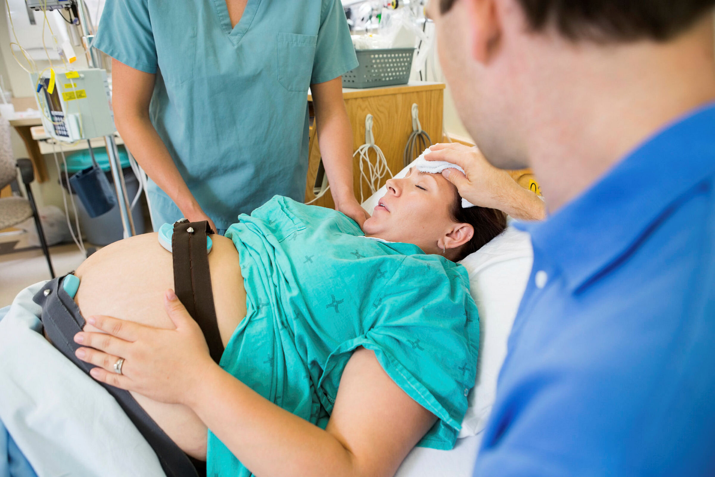 Bildet viser en kvinne som holder på å føde. Sykepleierne og legen måler fosterlyden, mens faren tørker pannen til kvinnen.