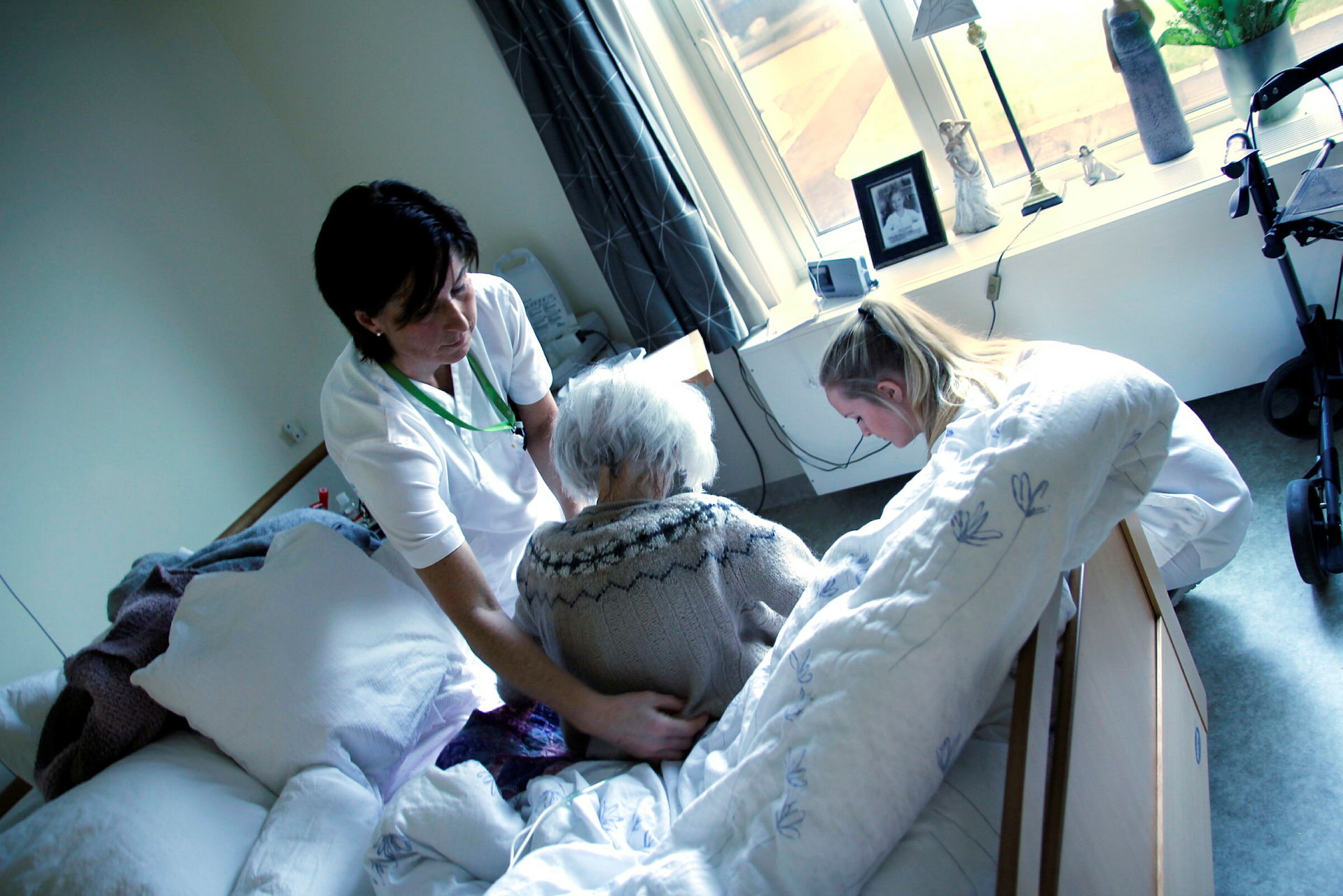 Bildet viser to sykepleiere som hjelper en pasient i sengen hennes på Karmøy sykehjem.
