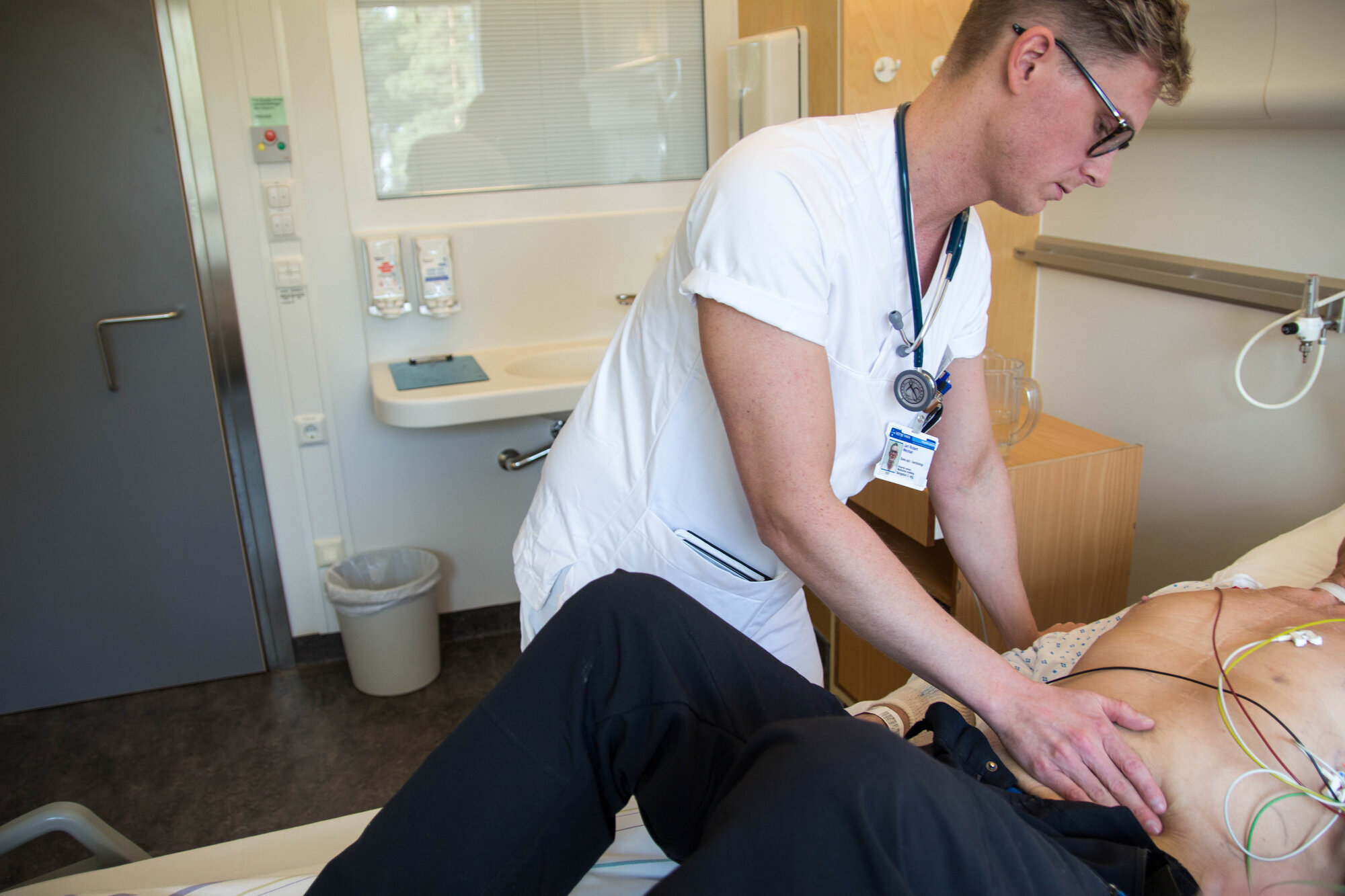 Bildet viser Jarl Robert Wexhall som palperer magen til en pasient.