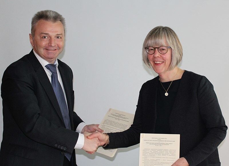 Anne Grethe Erlandsen og  Igor Kagramanyan gir hverandre et håndtrykk mens de holder programmet de har signert