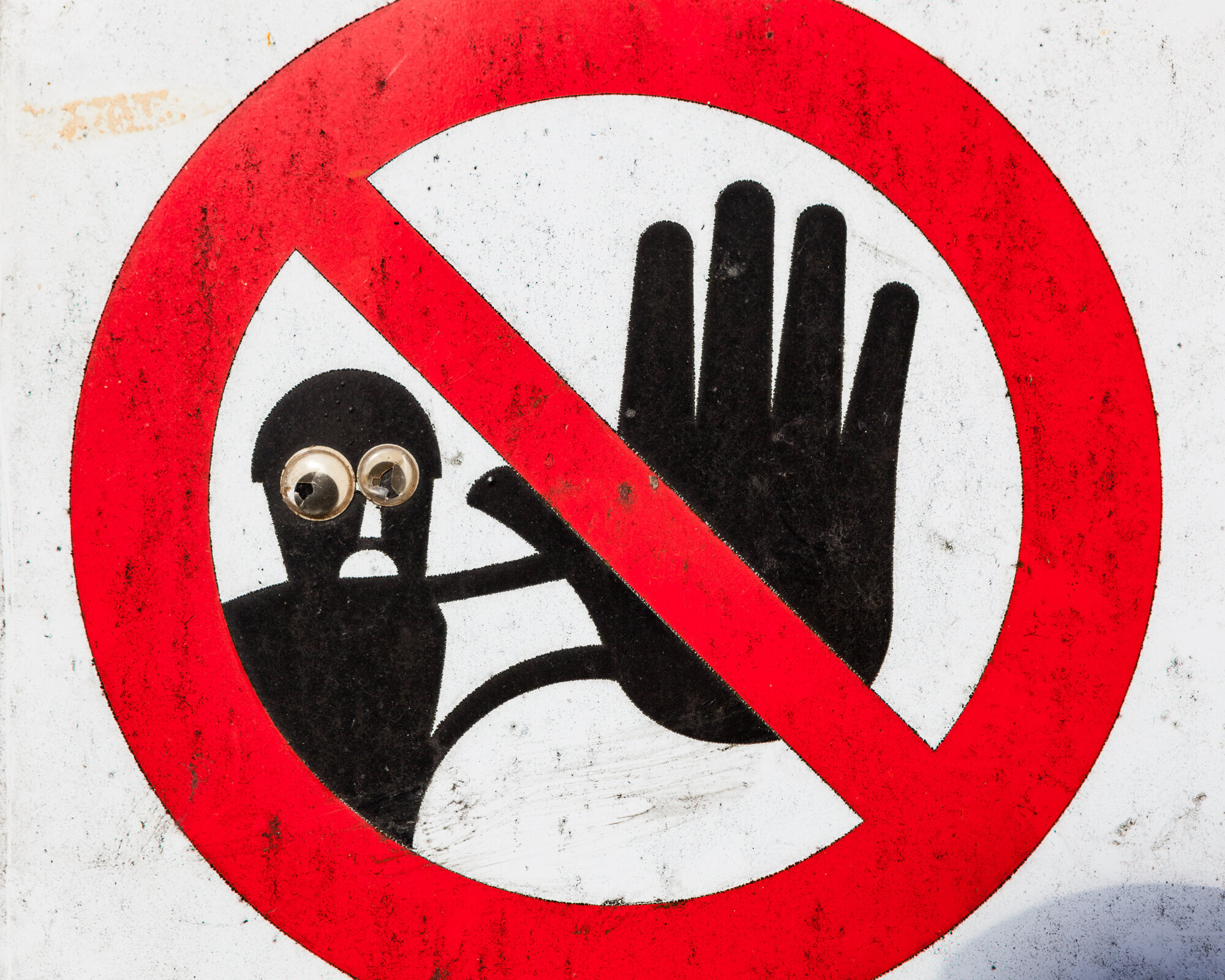 Bildet viser et forbudsskilt. En svart skikkelse i bakgrunnen viser stoppsignalet med håndflaten