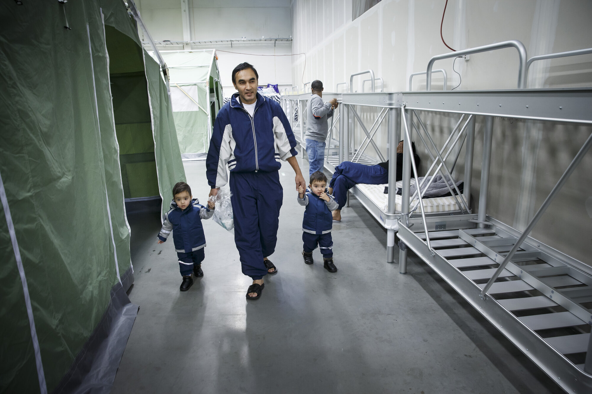 Bildet viser Gulam Sarwar og tvillingsønnene som går langs en rad med køyesenger på ankomstmottaket i Råde.