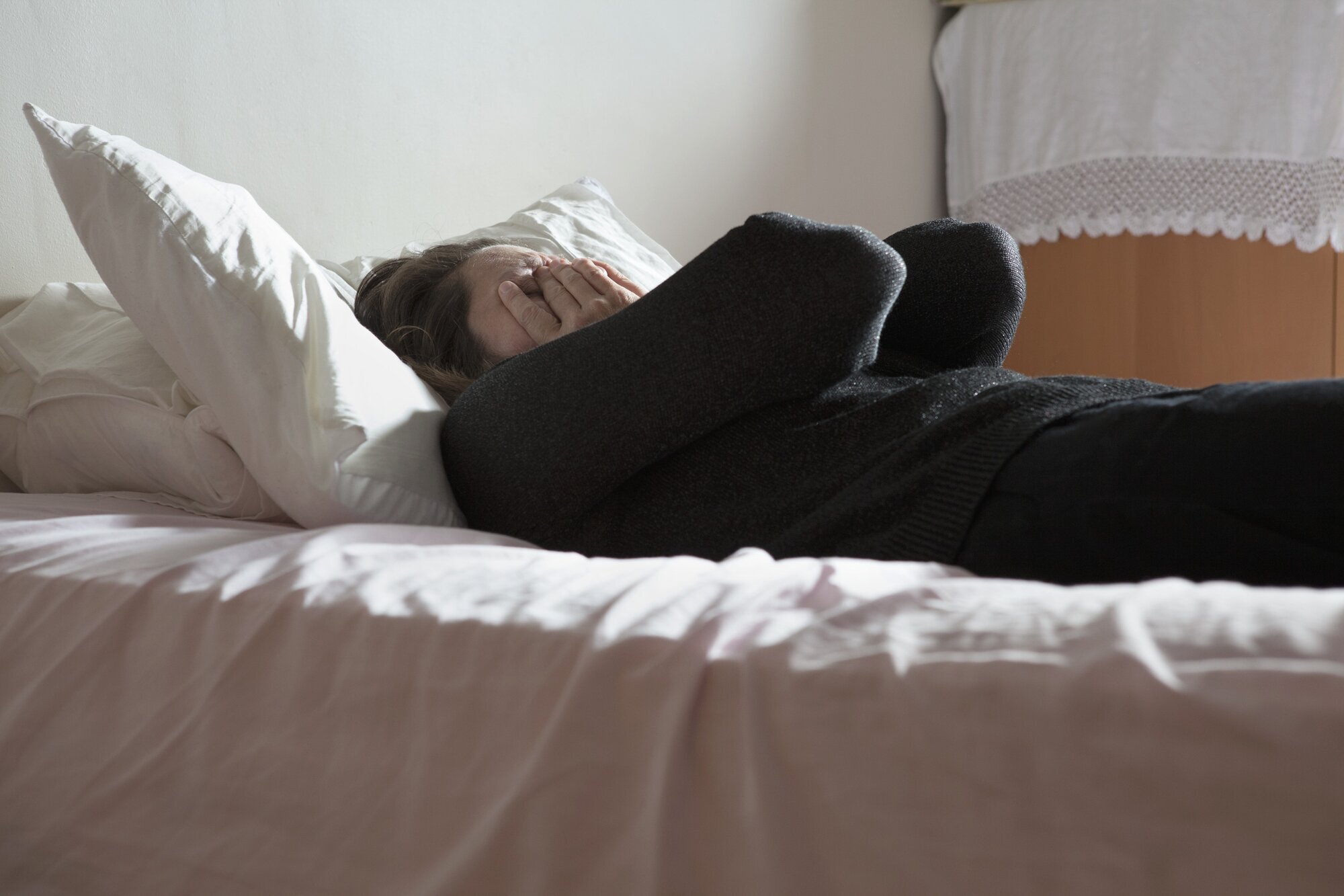 Bildet viser en deprimert kvinne som ligger på en seng og holder hendene foran ansiktet