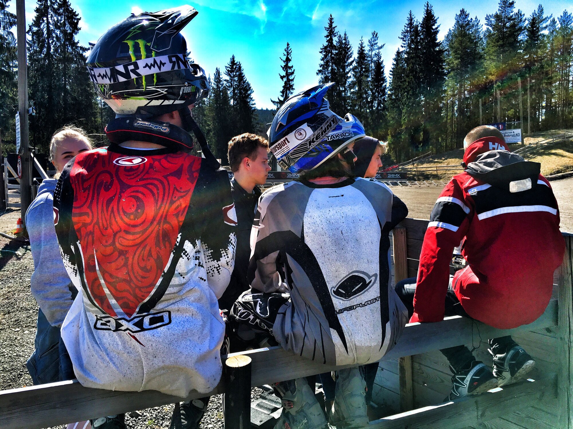 Bildet viser noen ungdommer som sitter på et gjerde med ryggen til og MC-hjelmer på hodet