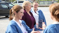 Bildet viser Ida Gerø med mobiltelefon, i bakgrunnen statsminister Erna Solberg og andre sykepleiere.