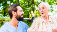 Bildet viser en mannlig sykepleier som snakker med en eldre dame. De sitter ute, og det er god stemning.