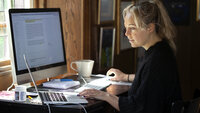 Bildet viser en kvinne som sitter hjemme ved en datamaskin.