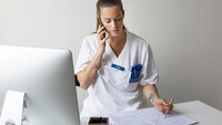 Bildet viser en ung, kvinnelig sykepleier som snakker i telefonen og tar notater.