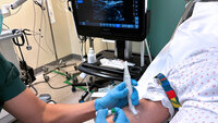 The photo shows a nurse using ultrasound to locate a vein before catheterisation