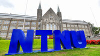 Bildeviser logoen til NTNU på gressplenen foran den gamle hovedinngangen 