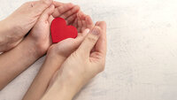 Bildet viser et par damehender som holdt rundt et par barnehender. Barnet holder et hjerte i sine hender.