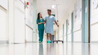 Bildet viser en sykepleier og en pasient som går i sykehuskorridoren sammen
