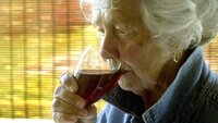Bildet viser en eldre kvinne som drikker rødvin
