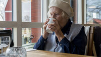 Bildet viser eldre kvinne som drikker av kopp