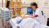 Bildet viser en simuleringsdukke på respirator. En sykepleier står lent over senga.