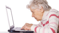 Bildet viser en eldre dame som sitter foran en datamaskin