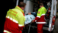 Bildet viser en mann som blir hentet av ambulansepersonale, og ligger på båre.