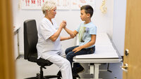 Bildet viser en eldre kvinnelige lege som undersøker en ung gutt.