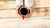 En kvinnes hender holder en kopp med kaffe på et rustikt trebord