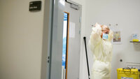 Smittefrakk Bildet viser en sykepleier som står i en sluse inn til et isolat og tar på seg gul smittefrakk.