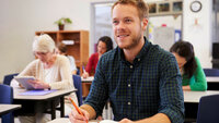 Bildet viser en ung mann i et klasserom. Det er flere studenter også i bakgrunnen.