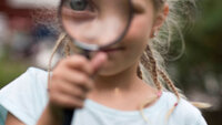 Bildet viser en jente som ser gjennom et forstørrelsesglass.