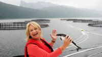 Torill er ute ved et fiskeoppdrettsanlegg. Hun holder en fisk i hånden.