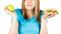 Matvalg En jente holder en hamburger i ene hånden og ett eple i den andre. Valgets kval