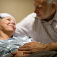 Bildet viser eldre mann ved sykeseng til kona