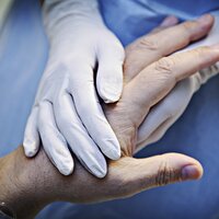 Bildet viser et par hender med plasthansker som holder hånda til en gammel person