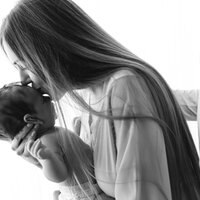 Bildet viser en mor som holder sitt spedbarn i armene mens hun kysser barnet på hodet. Mannen hennes holder rundt henne.