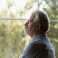 Bildet viser en eldre mann som titter ut av vinduet. Han ser tankefull og bekymret ut