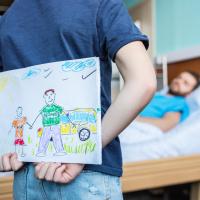 Barn gjemmer tegning bak ryggen ved fars sykeseng.