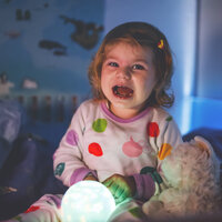 Bildet viser ei lita jente som sitter gråtende i senga. Foran seg holder hun ei lyslampe