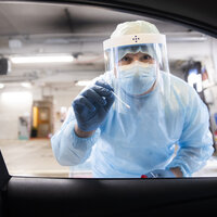 Bildet viser en helsearbeider i smittevernutstyr som holder frem en testpinne.