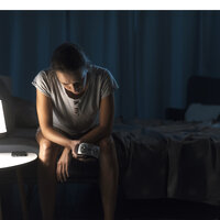 Bildet viser en kvinne som sitter på sengekanten og ikke får sove