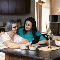 Bildet viser et helsepersonell som holder rundt en eldre kvinne som ser på et nettbrett