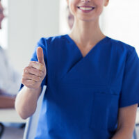 Bildet viser en sykepleier i front som viser "tommel opp" mens hun smiler.