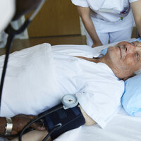 Bildet viser en sengeliggende mannlig pasient som får pleie av to sykepleiere