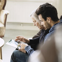 Bildet viser en eldre dame på sykehjem som ser på et nettbrett sammen med en pleier