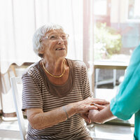Bildet viser en hjemmeboende eldre kvinne som smiler til en sykepleier.