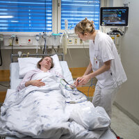 Bildet viser en sykepleier som står ved sengen til en pasient på sykehus