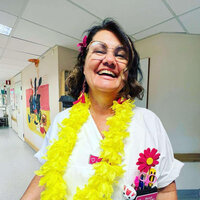 Sykepleier på jobb. hun har blomster rundt halsen og smiler.