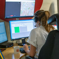 Bildet viser en telefonoperatører som sitter på legevaktsentralen i et "avlukke" foran mange skjermer