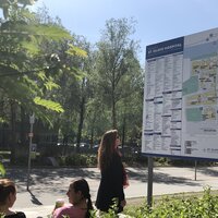 Bildet viser en dame som står foran et digert skilt foran St. Olavs hospital. Skiltet viser informasjon om sykehuset