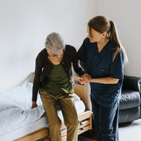 Bildet viser en sykepleier som hjelper en pasient opp av sengen