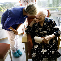 Bildet viser en eldre kvinne på velferdssenter. Får omsorg fra en av de ansatte.