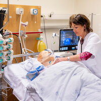 Bildet viser en simuleringsdukke på respirator. En sykepleier står lent over senga.