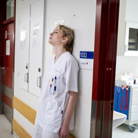 Bildet viser en sliten sykepleier som er lent mot veggen med ryggen.